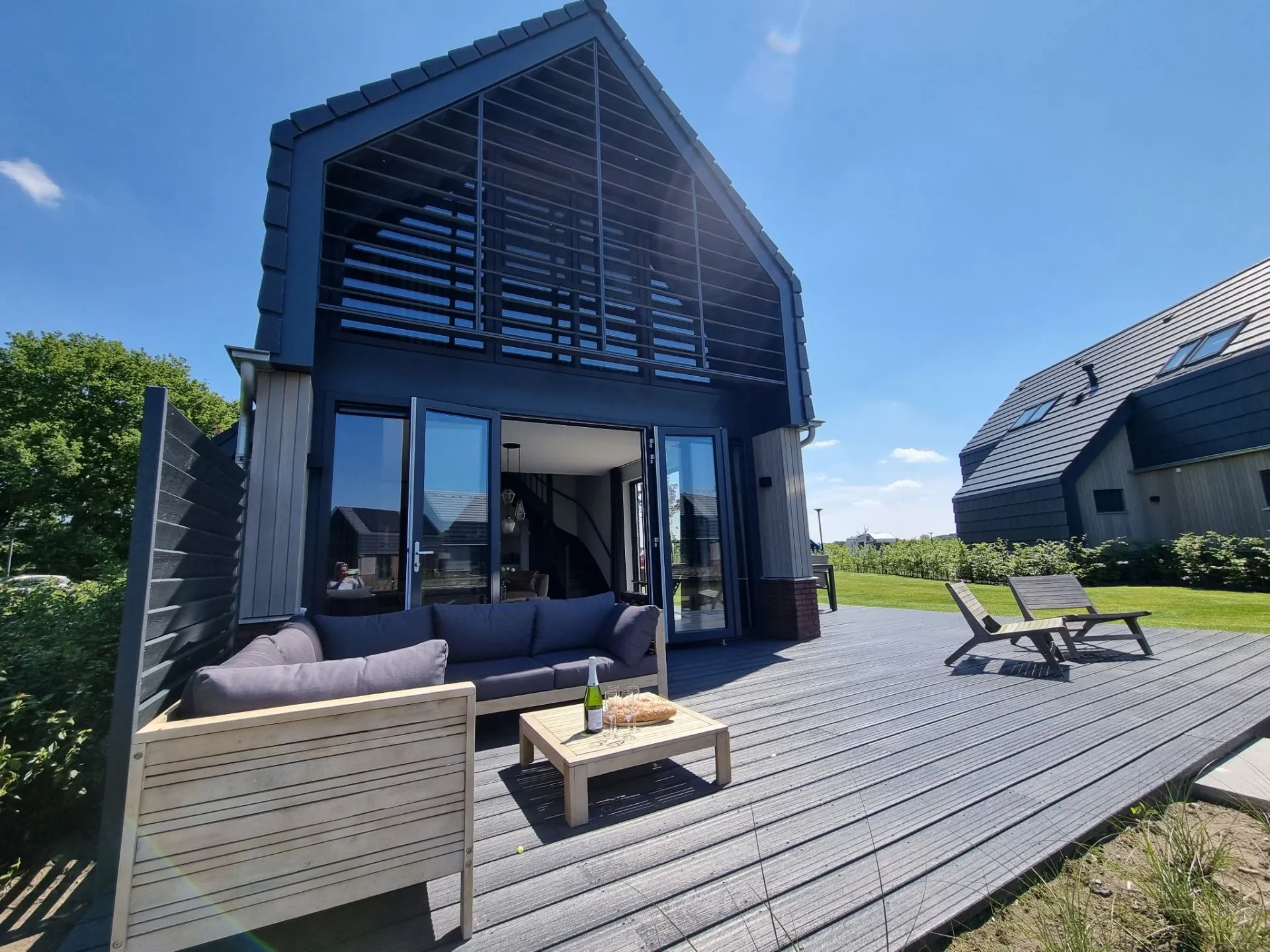 Hoge moderne woning met veel zwart en hout en zwarte kunststof openslaande deuren