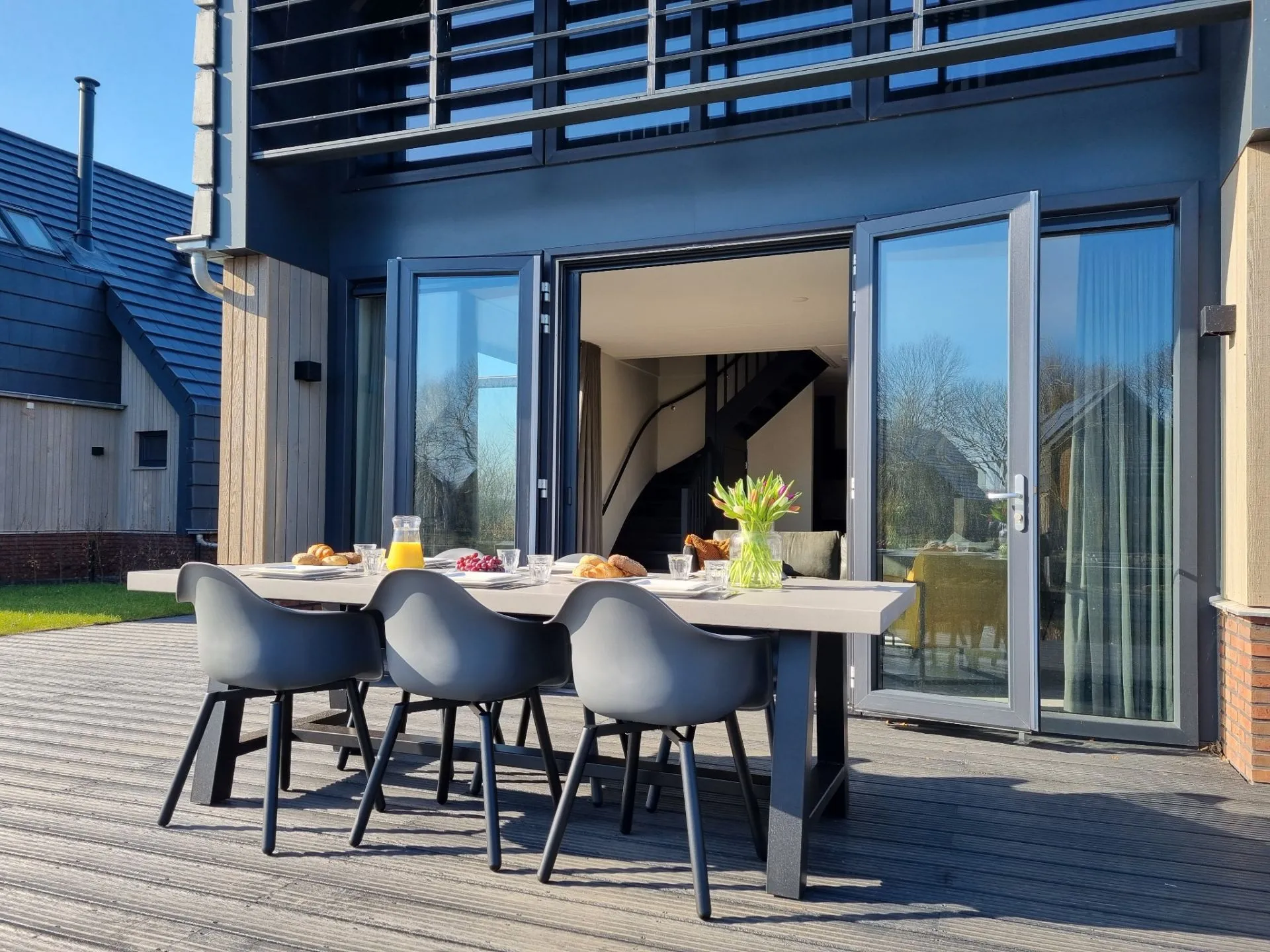 Woning met hout en zwarte kunststof openslaande deuren en een dining tuinset ervoor